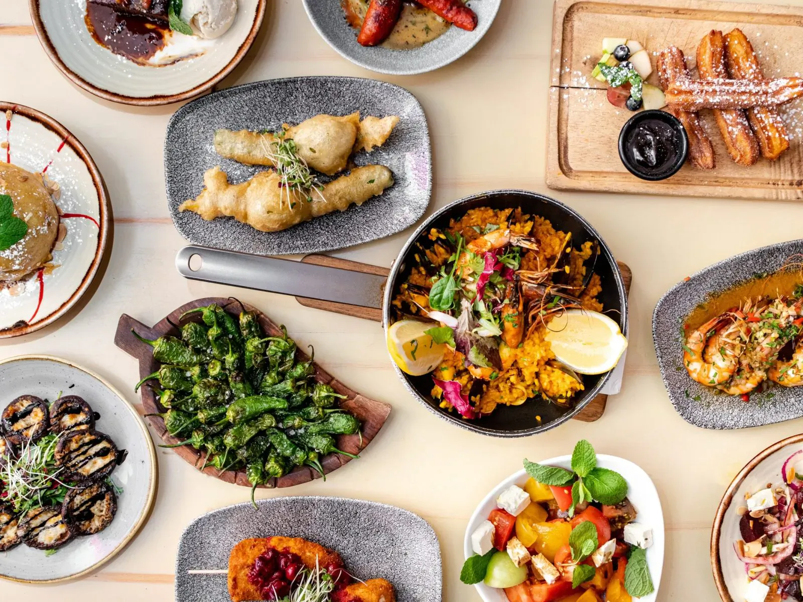 Overhead view of Spanish tapas: paella, prawns, sausages, fried fish, veggies on plates