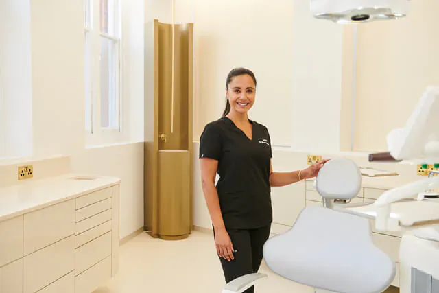 Smiling female dentist in black scrubs standing beside dental chair in modern clinic