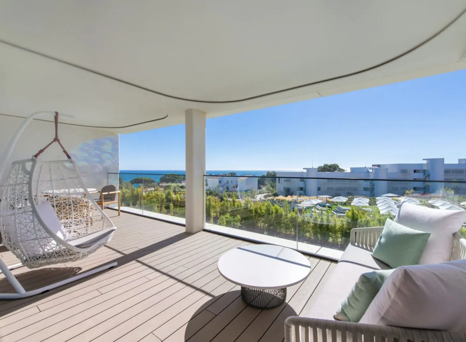 Spacious modern balcony at W Algarve Hotel with white hanging egg chair, green cushions on lounge seats, round table, and ocean view.