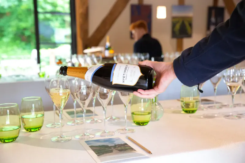 Hand pouring Nyetimber English sparkling wine from bottle into glasses on table at gallery event