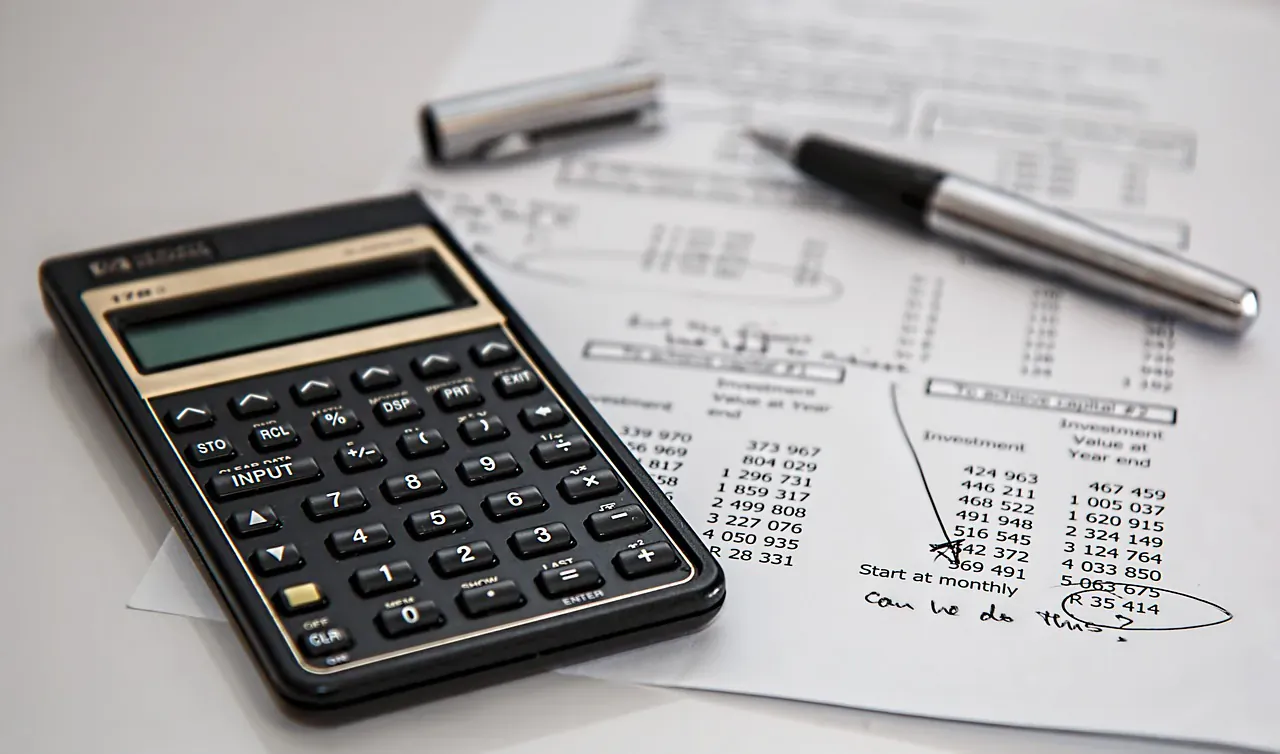 Black calculator on financial papers with numbers and handwritten 'Quels sont les frais?' next to pens
