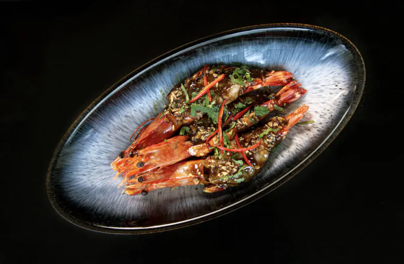 Stir-fried prawns with red chilies and Thai herbs on a dark oval plate