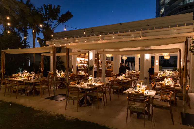 Twilight patio dining at Continuum with candlelit tables, palm trees, string lights, and patrons for South Beach Wine & Food Festival BBQ Marvel