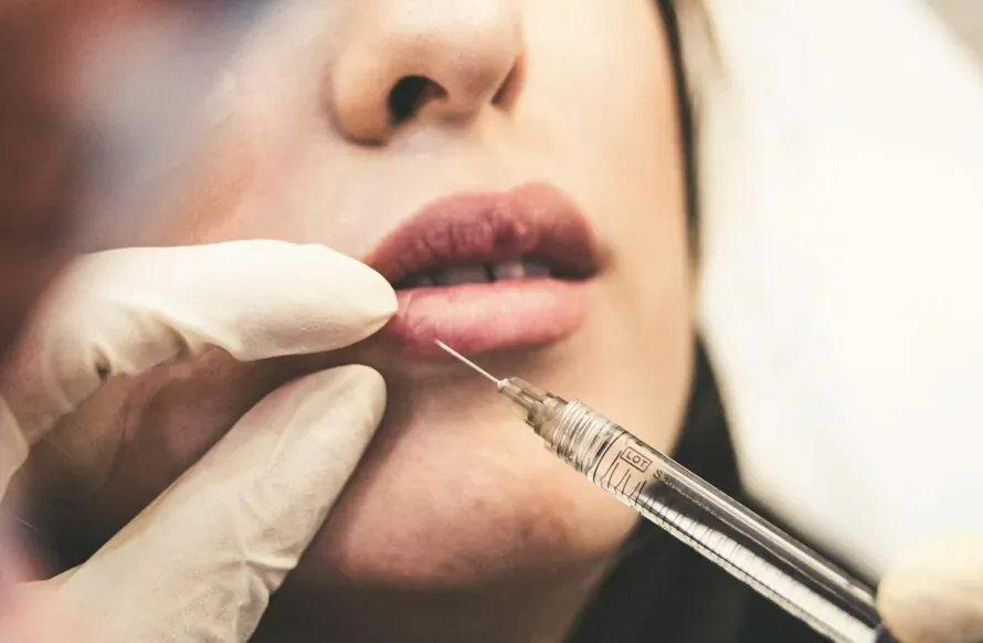 Close-up of gloved hand injecting syringe into woman's plump lips during cosmetic procedure