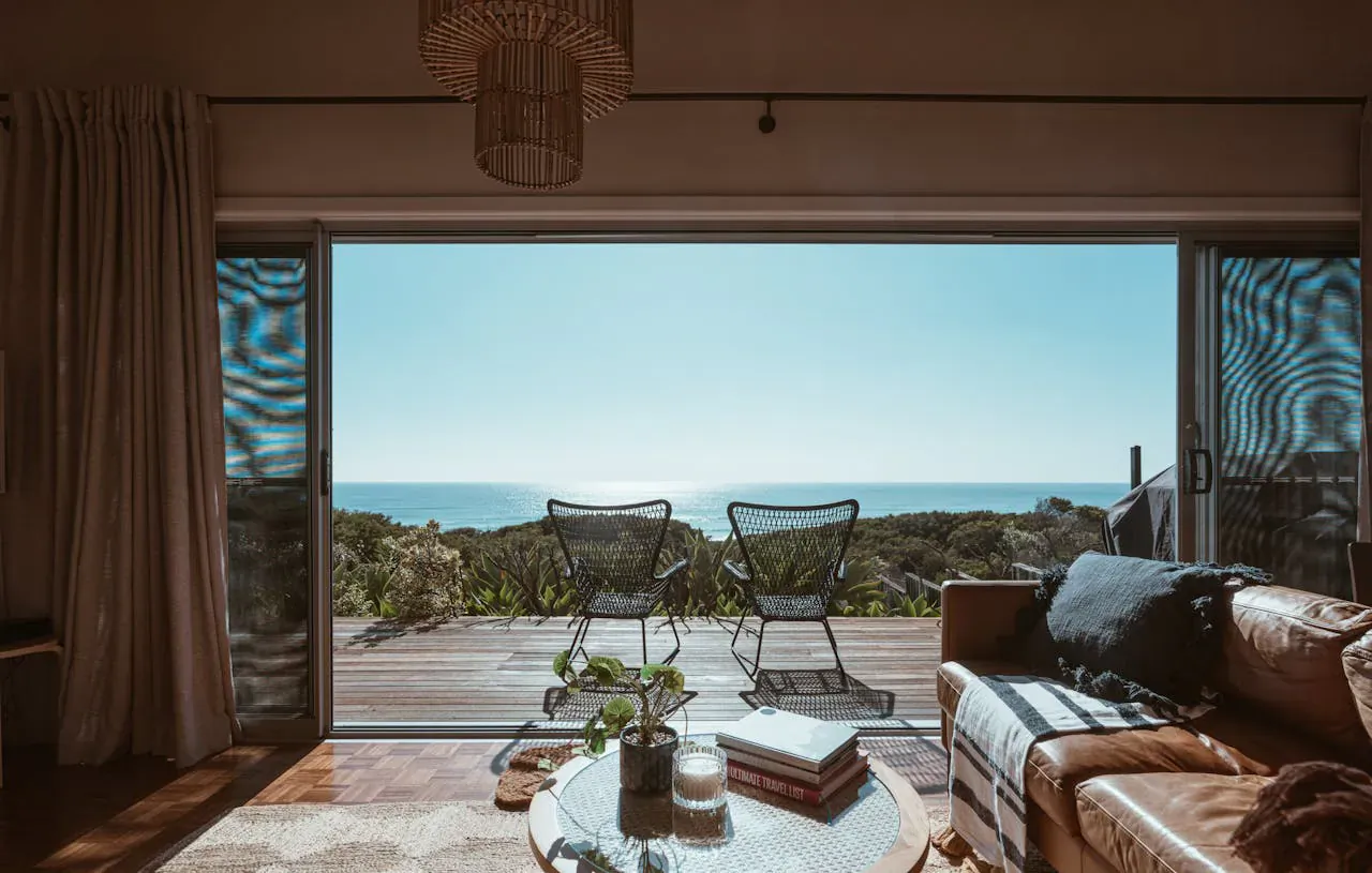 Cozy cabin interior with open doors to deck, rattan chairs, leather sofa, coffee table, and ocean view.