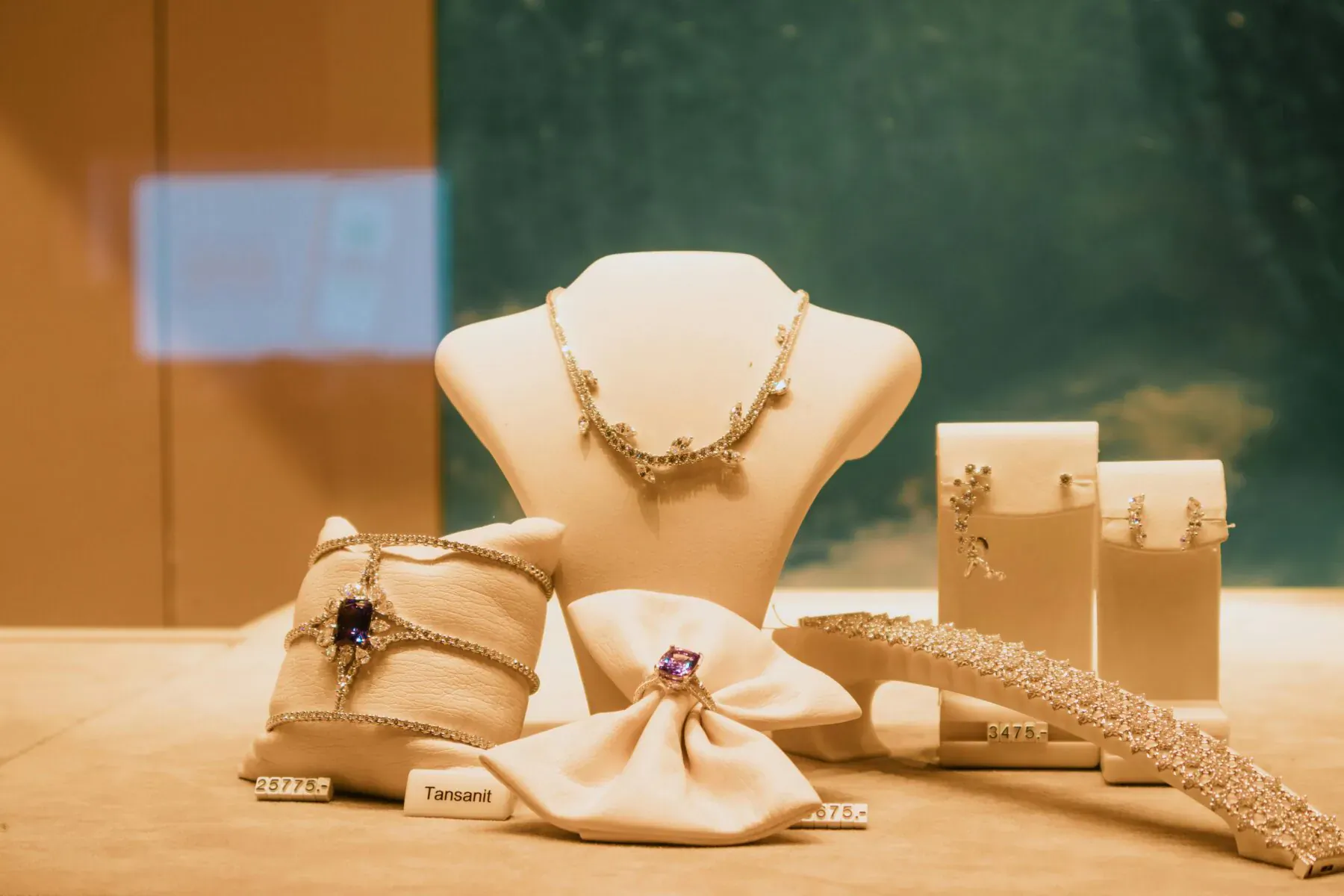 Luxury jewelry display on glass case: purple gem bracelet and necklace on white mannequin, earrings, and 'Taffin' label.
