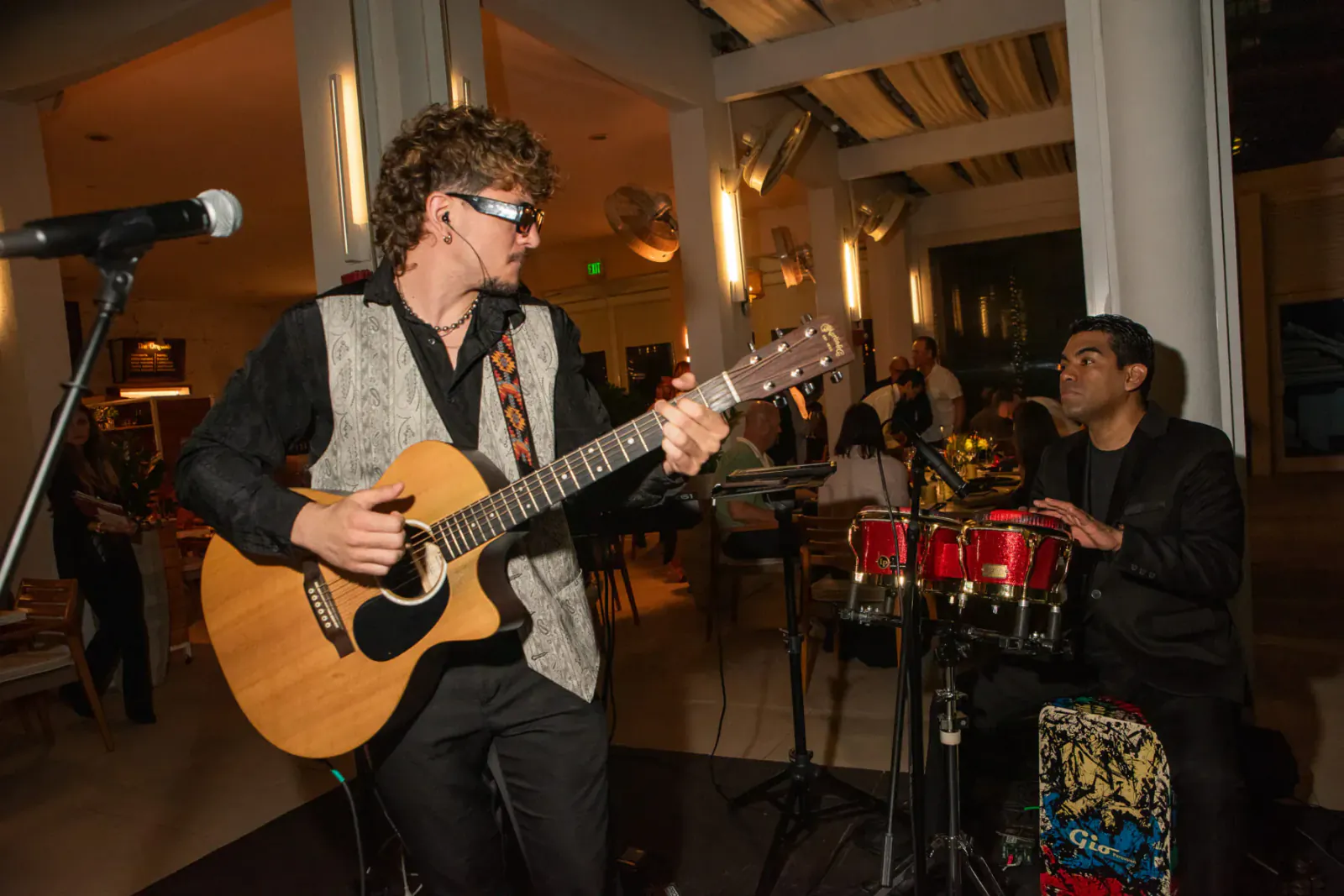 Pat Martin with shaggy hair and shades strums acoustic guitar on stage with drummer at food festival