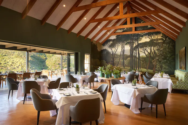 Elegant dining room at Brookdale Wine Estate with wooden beams, vineyard mural, tables set, and Paarl valley view.