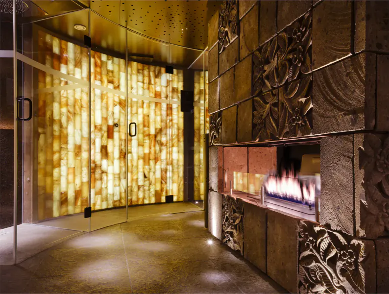 Elegant wellness gallery interior with glowing onyx walls, carved stone fireplace with flames, and glass doors.