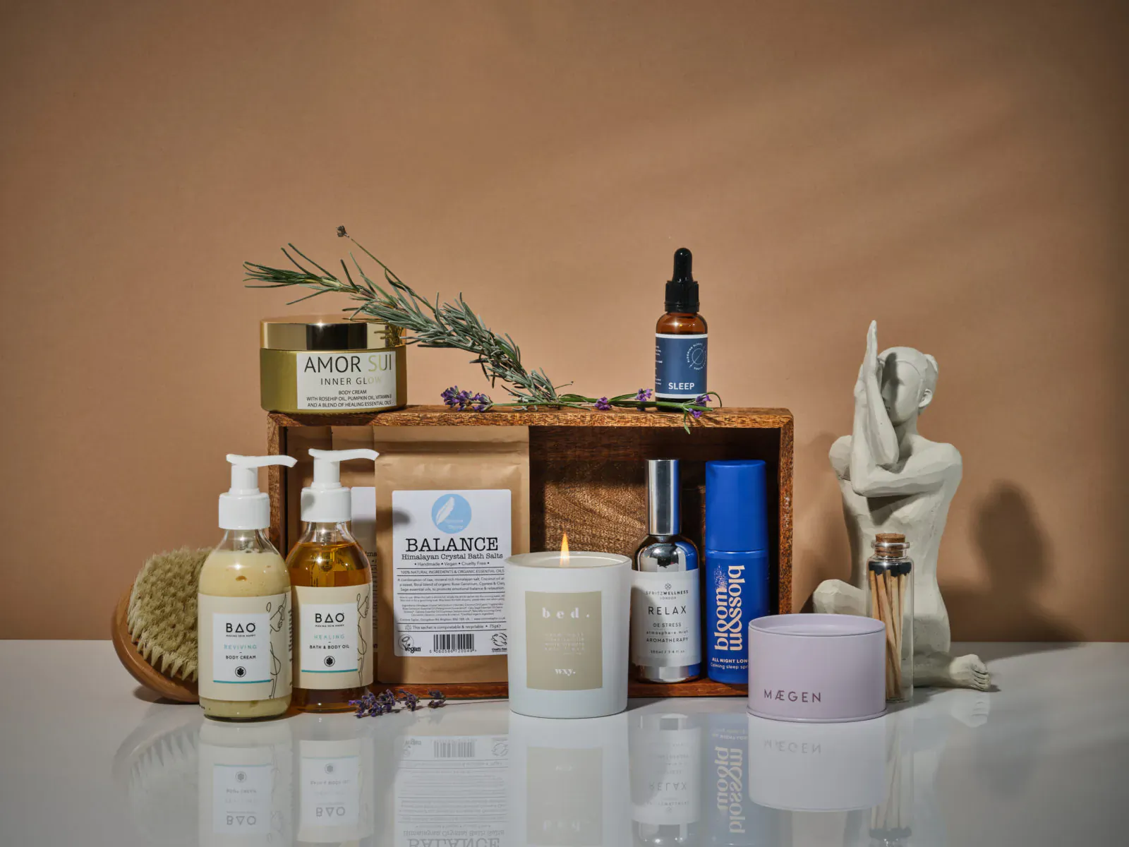 Assortment of sustainable skincare products like Amour, Balance jars, serums, candle on wooden surface with greenery and statue.