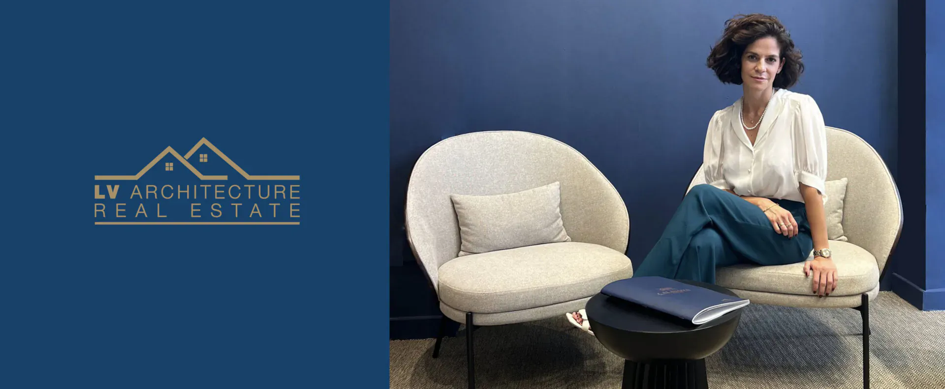 Vanessa Moreno, LV Arquitectura Real Estate Sales Director, seated smiling in white blouse on blue chair beside logo