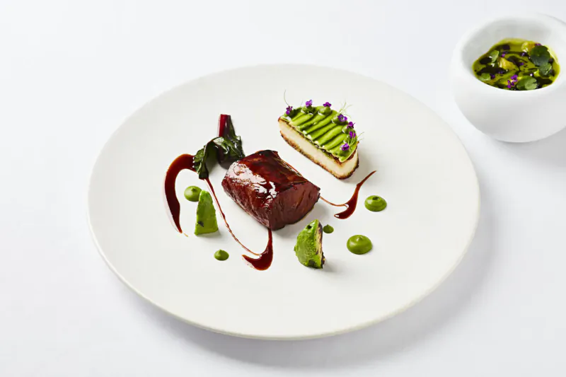Elegant plate of roasted beet with green herb sauce, piped cream cake, and garnishes