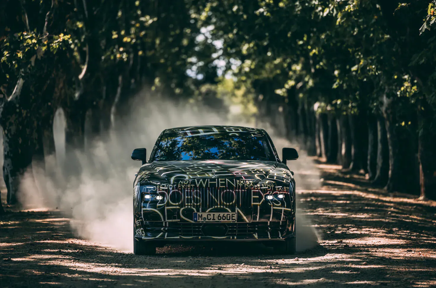 All-electric Rolls-Royce Spectre with 'DOES NOT APPLY' graffiti speeding on tree-lined path, kicking up dust during testing.