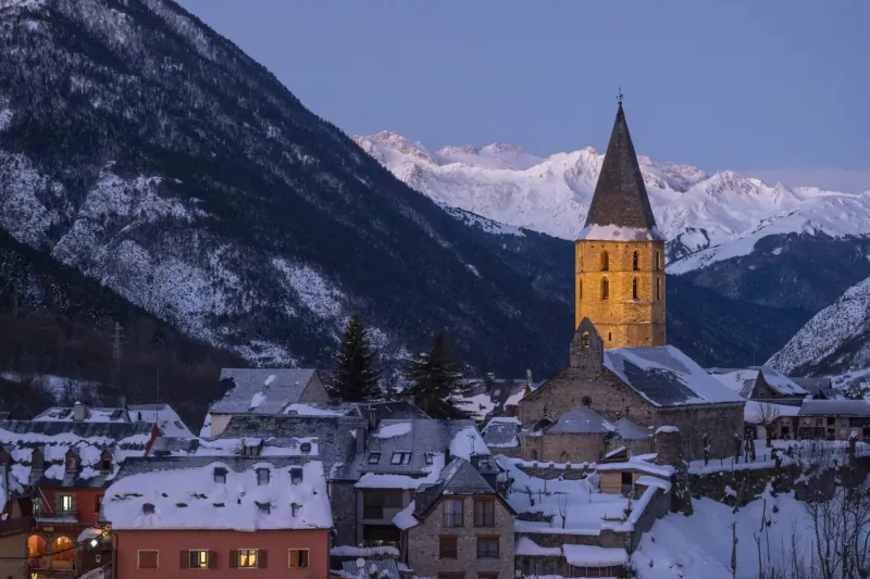 Golden church tower in snowy Val d'Aran village, Pyrenees mountains at dusk