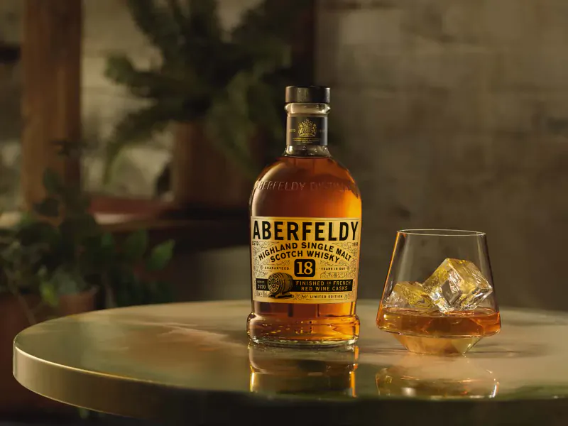 Aberfeldy 12 Year Old Single Malt Scotch Whisky bottle beside a glass of whisky with ice on a table.