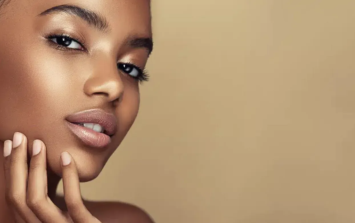 Close-up portrait of a beautiful Black woman with glowing skin, touching her face, warm beige background