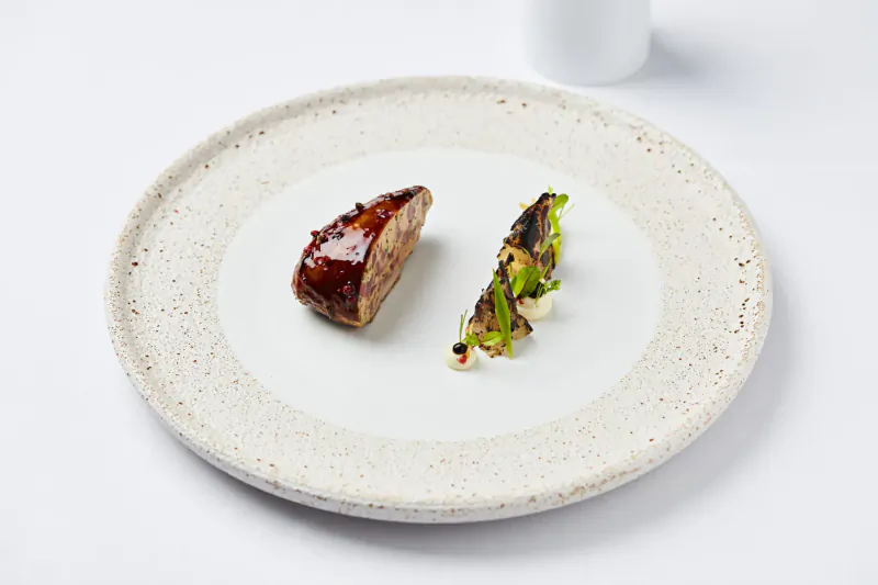 Close-up of glazed roasted meat slice and charred green vegetables on white plate
