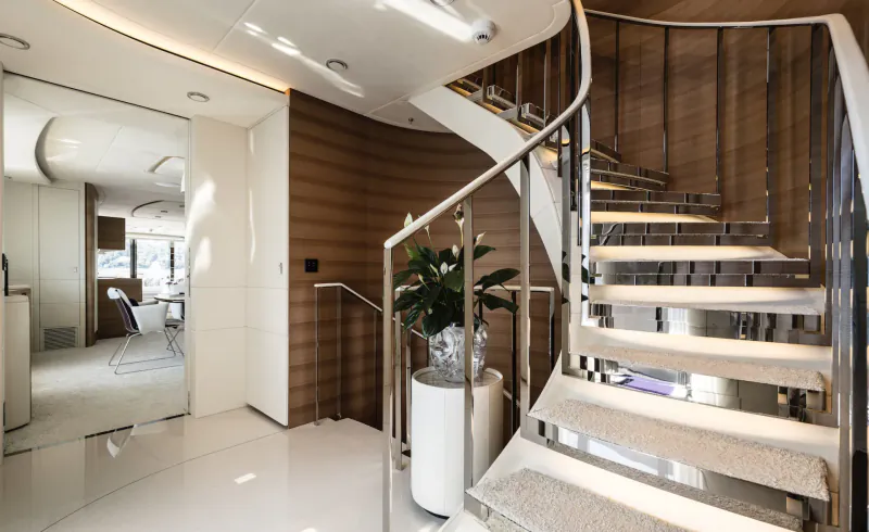 Elegant curved wooden staircase with chrome railing and potted plant in luxurious yacht interior