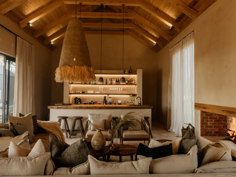 Cozy living area in Savanna luxury villa with rattan pendant light, kitchen island, plush sofa, and fireplace.