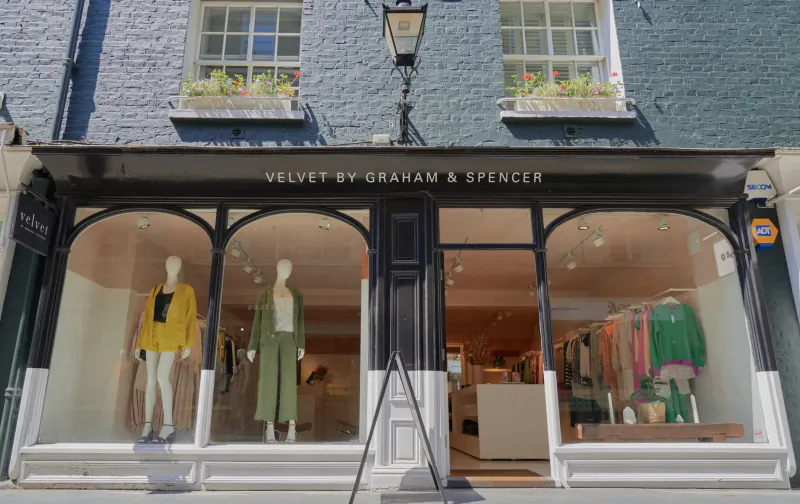 Velvet by Graham & Spencer boutique storefront on Georgian building with mannequins in yellow and green outfits in windows.