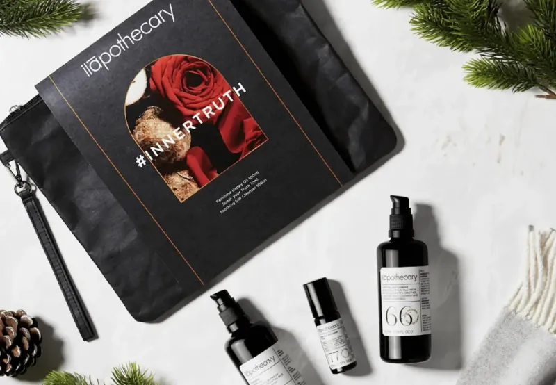 ID Apothecary #InherentTruth luxury skincare gift set with black pouch, rose motif, serum bottles, and holiday pine accents