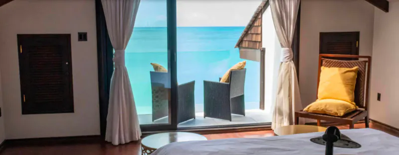Luxury bedroom at Tamarind Hills with yellow armchairs on balcony overlooking turquoise sea.