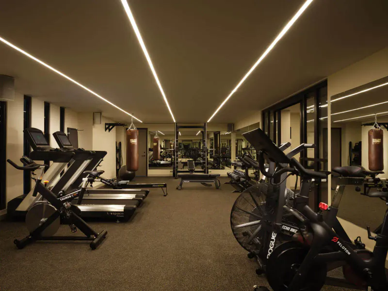 Spacious modern hotel gym with treadmills, exercise bikes, weight bench, punching bags, mirrors, and LED lighting.