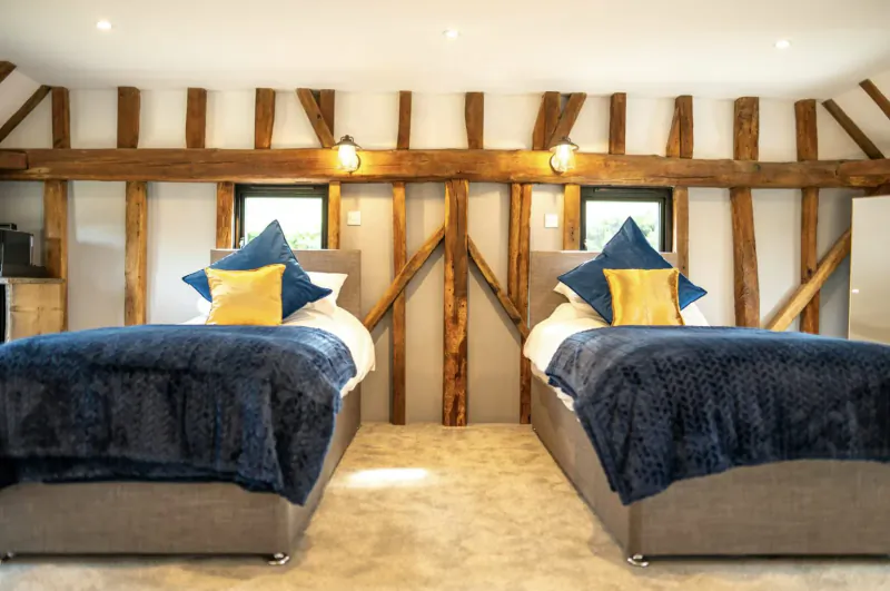 Two luxurious twin beds with navy duvets and yellow pillows in a beamed barn room at Chart Hills.
