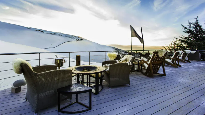 Luxury lounge area with cushioned chairs, fire pit, and German flag on snowy Sierra Nevada mountain deck at sunset.