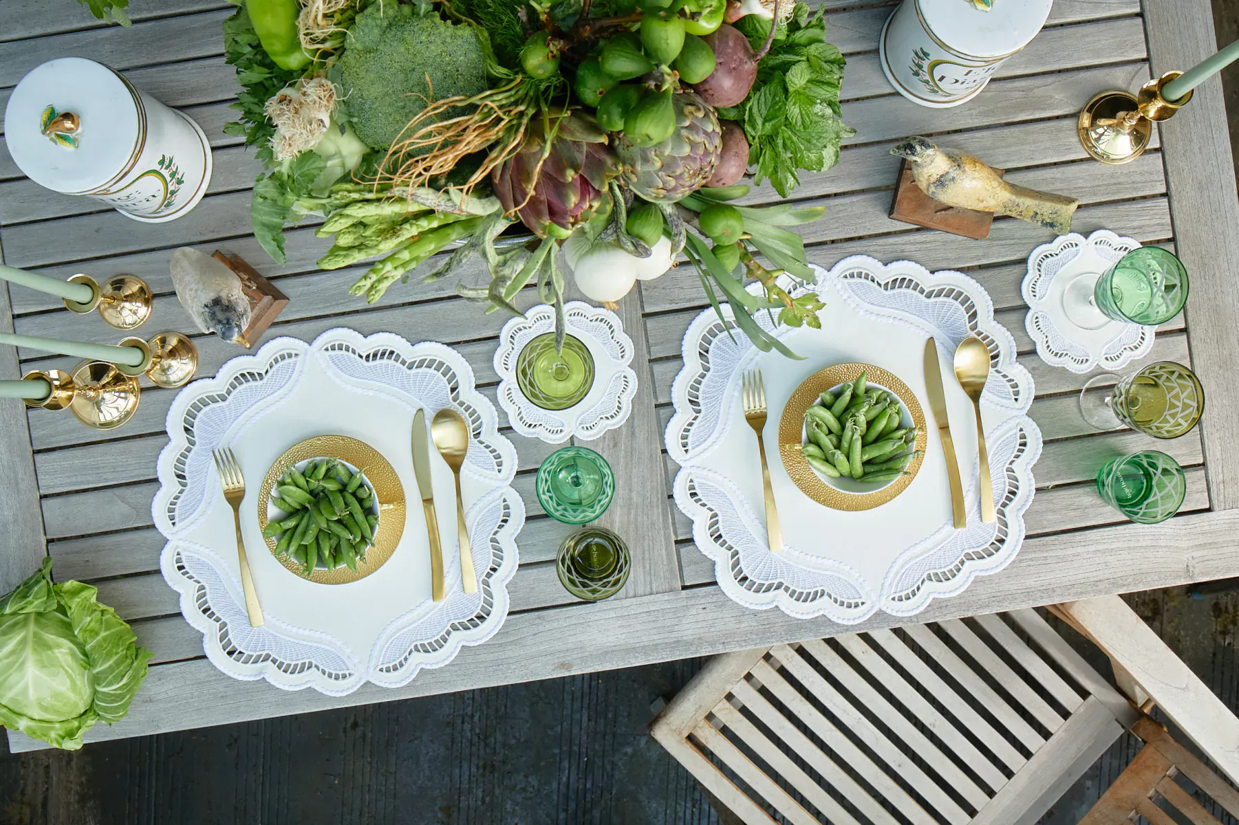 Overhead view of two luxury Truffle Bee table settings with white scalloped plates, green veggie salads, gold utensils, and lush green centerpiece on wooden table.