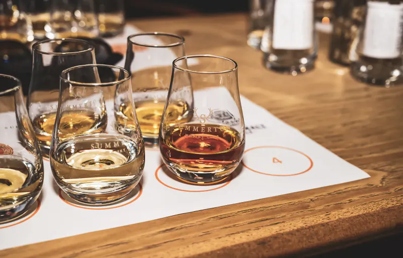 Whisky tasting flight with clear, yellow, and amber drams in Glencairn glasses on wooden table at Summerton Whisky Club