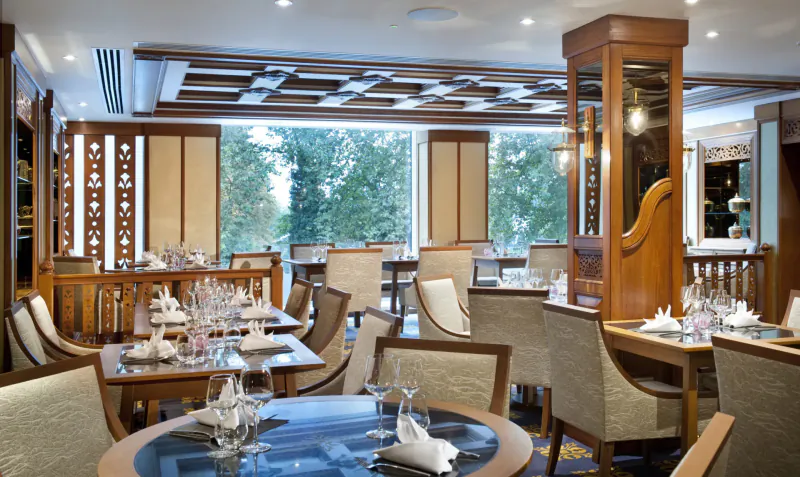 Elegant Nipa Thai restaurant interior with wooden decor, set tables with glassware, and garden view windows.