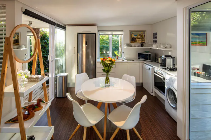 Bright modern kitchen in Spanish Farm Guest Lodge with round white table, chairs, yellow flowers, and garden view.