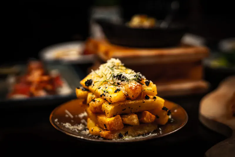 Stack of golden fried cheese curds topped with grated cheese on a plate, surrounded by Anatolian dishes