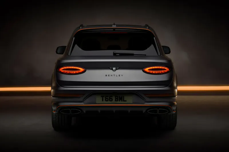 Rear view of black Bentley Bentayga SUV with glowing taillights, license plate TGB DRL, on dark road.