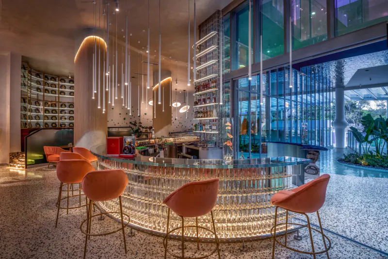 Modern curved bar with orange chairs, pendant lights, shelves of bottles, and poolside view at Gem Forest Hotel Nairobi MGallery.