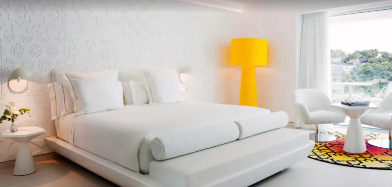 Elegant white bedroom by Marcel Wanders at Grand Hotel Portals Nous, yellow lamp, ocean view balcony.