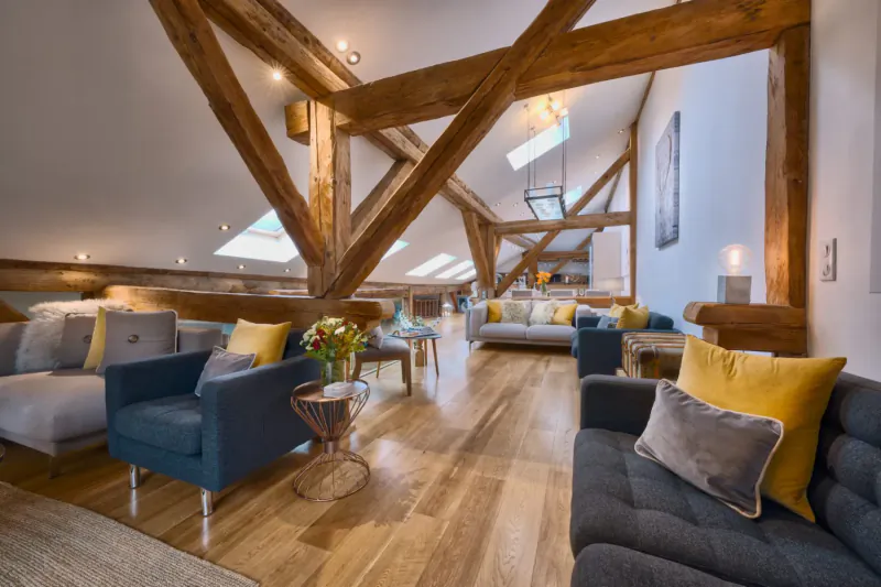 Spacious mountainside chalet loft with exposed wooden beams, skylights, plush sofas, and vase of flowers.