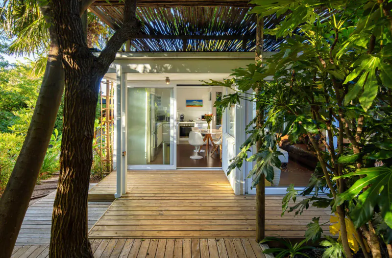 Modern wooden guest lodge with sliding glass doors open to deck, surrounded by lush green trees at Spanish Farm Guest Lodge.