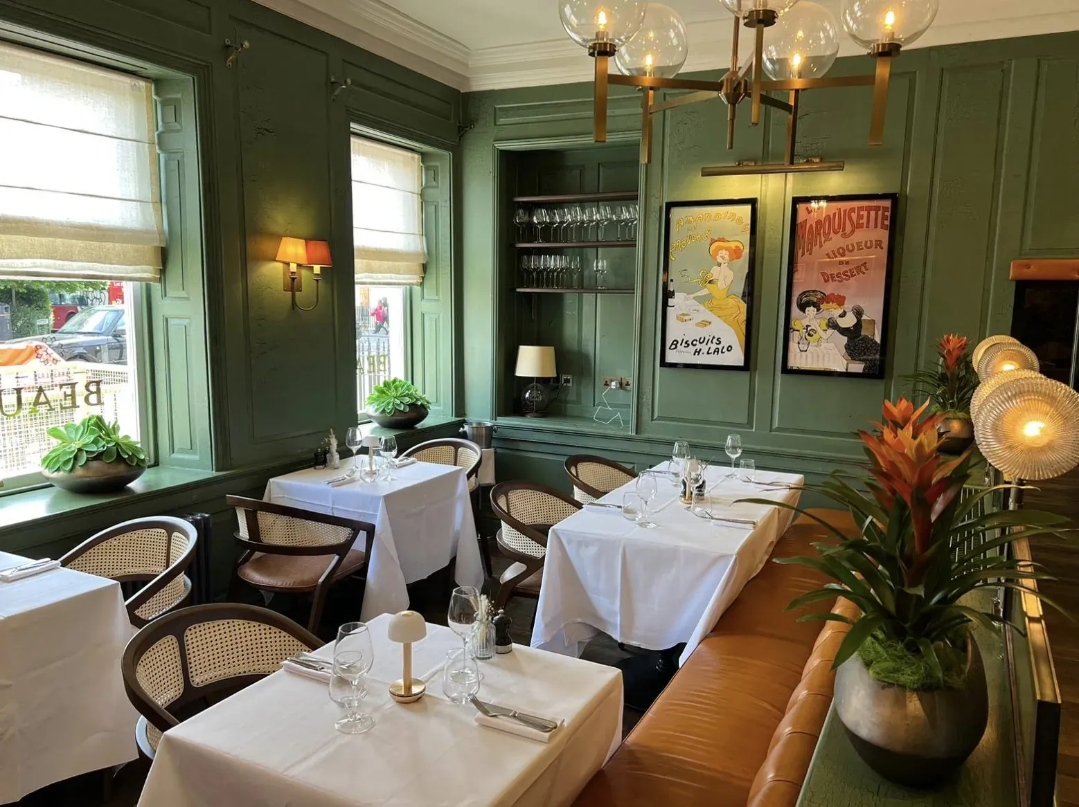 Elegant green-walled Brasserie Beau Bath dining room with white-clothed tables, rattan chairs, plants, and Toulouse-Lautrec posters.