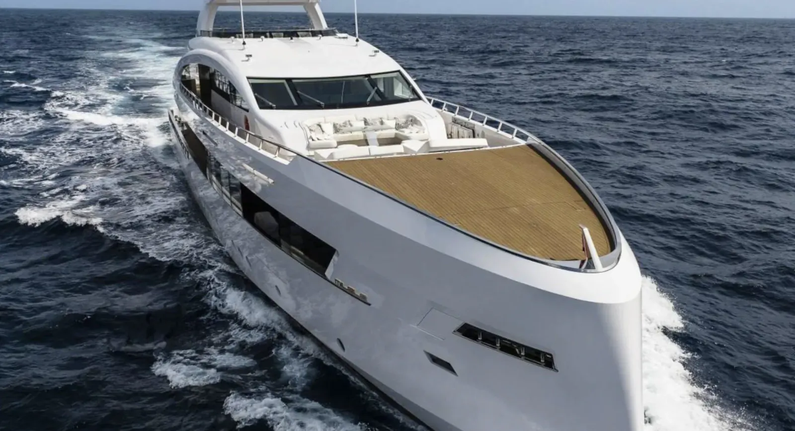 White luxury yacht Milele speeding on ocean, with teak deck and wake trailing behind.