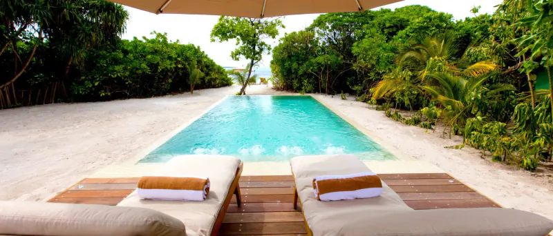 Two loungers with towels by infinity pool at tropical beach resort, Maldives, lush greenery backdrop