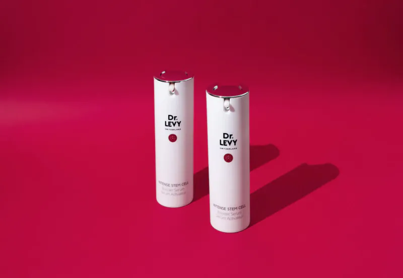 Two white Dr. Levey serum bottles with red caps on red background