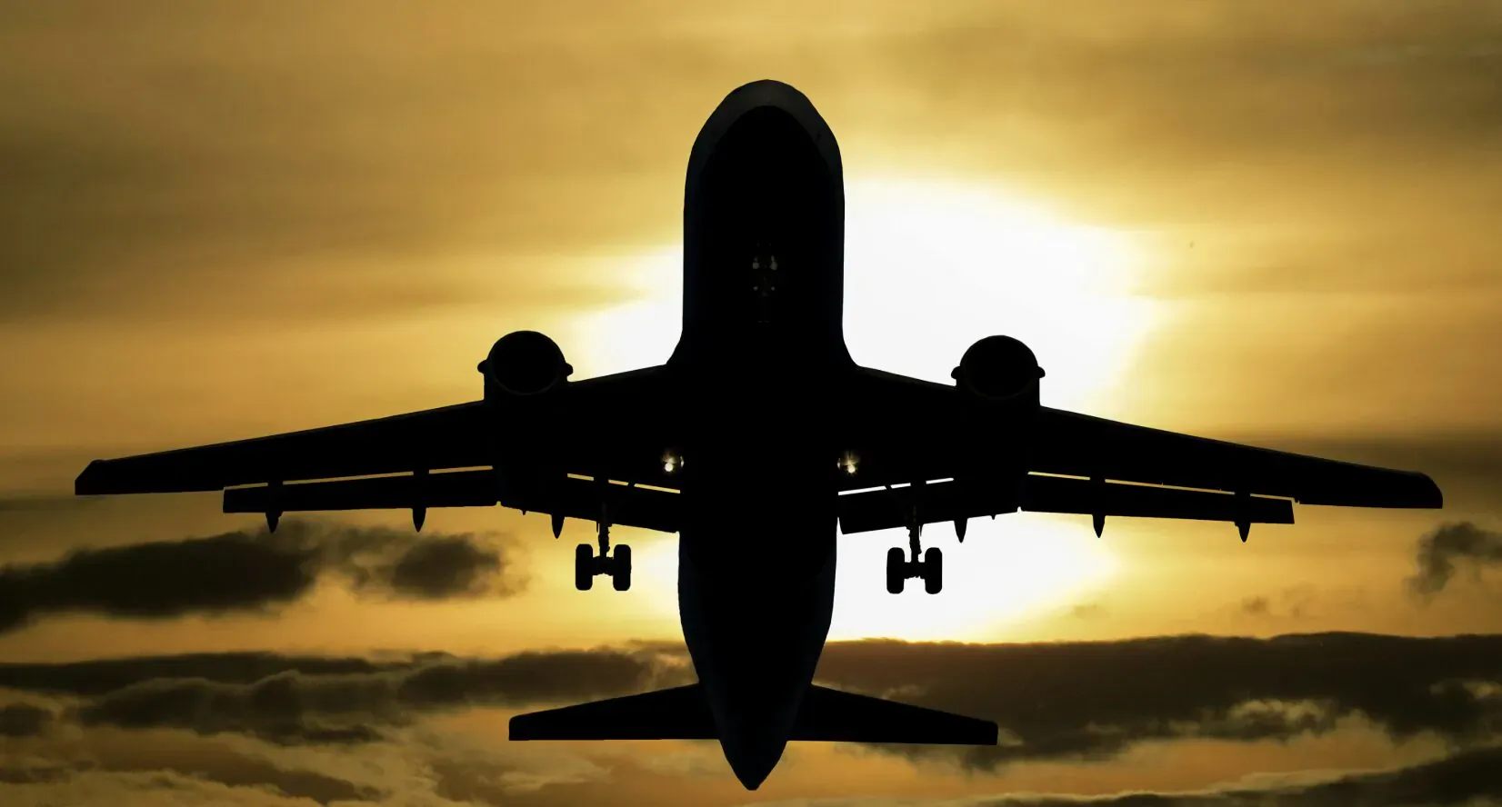 Silhouette of easyJet airplane flying towards glowing sunset with clouds