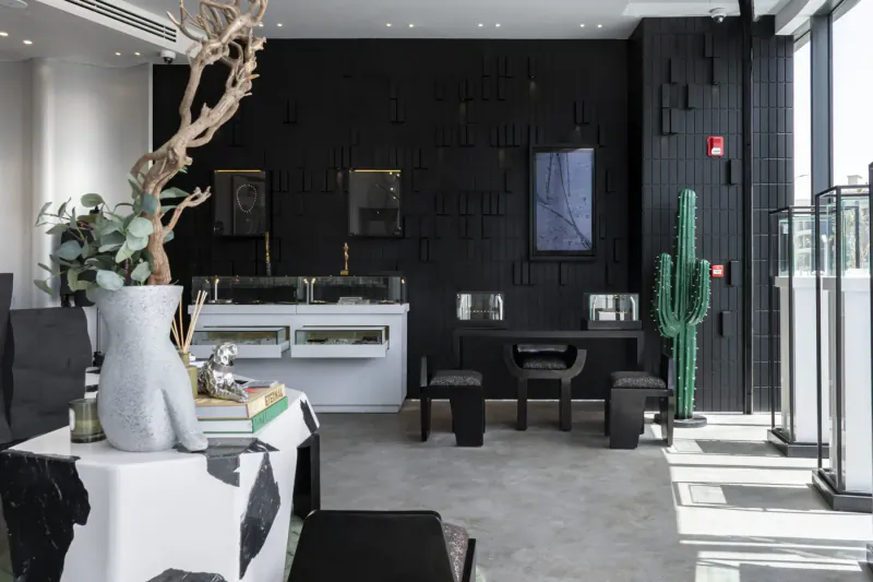 Modern men's jewelry flagship store interior in Cairo: black textured walls, white counters with displays, cactus, branches, eucalyptus.