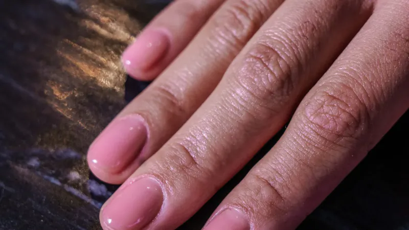 Close-up of hands with glossy pink nails on wooden surface at Urban Retreat London City