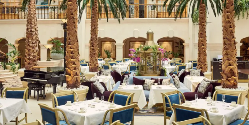 Elegant Winter Garden atrium at The Landmark with palm trees, ornate fountain, grand piano, and white-clothed dining tables.