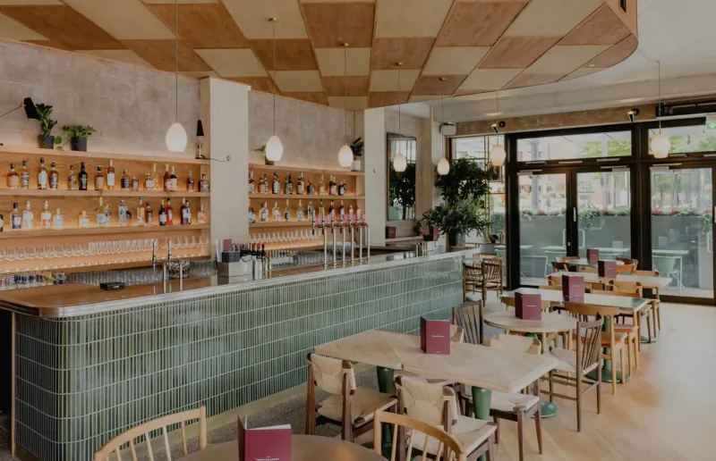 Sophisticated interior of The Broadcaster restaurant in London with wooden bar, green tiles, tables, and panoramic windows