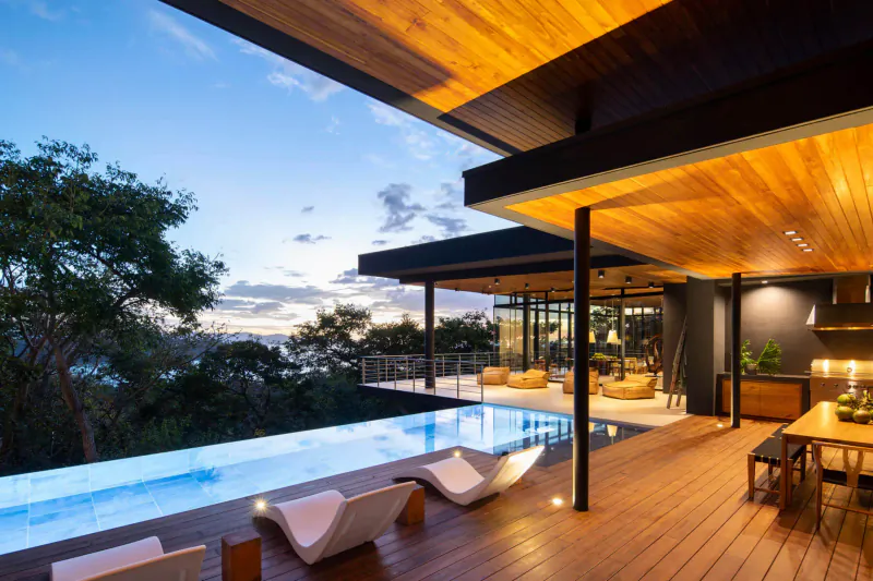Luxury modern home with infinity pool, wooden deck, lounge chairs, and sunset ocean view from SARCO Architects.