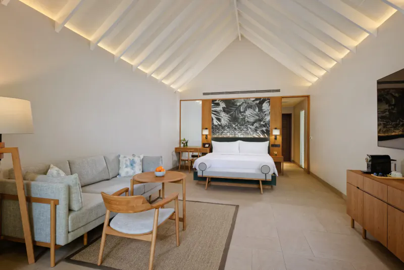 Luxurious Maldives villa bedroom with king bed, gray sofa, wood table, lamp, and abstract wall art